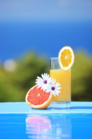 Glass of orange juice and flowers next to a swimming poolの写真素材