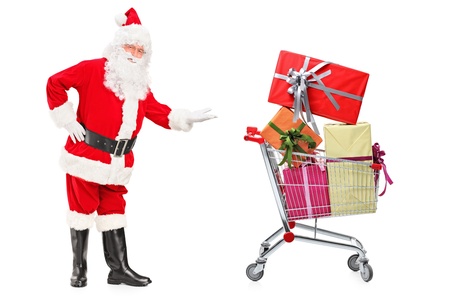 Full length portrait of a Santa Claus showing a shopping cart full of presents isolated on white backgroundの写真素材