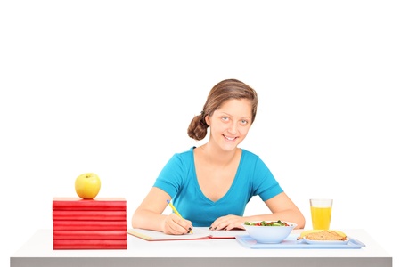 A smiling schoolgirl doing her homework isolated against white backgroundの写真素材