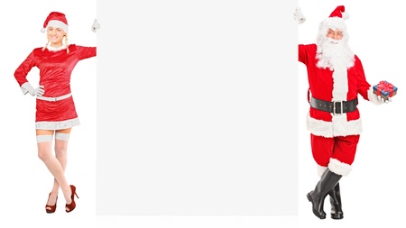 Full length portrait of a female and male Santa Clauses holding a white panel isolated on white backgroundの写真素材