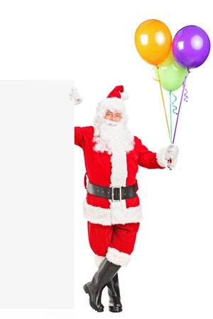 Full length portrait of a happy Santa claus standing next to a blank billboard and holding balloons isolated on whiteの写真素材