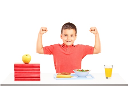 Strong boy showing his muscles and food on table during a breakfast isolated on white backgroundの写真素材