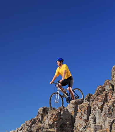 Person riding a mountain bike on rocks on a sunny day against a blue skyの写真素材