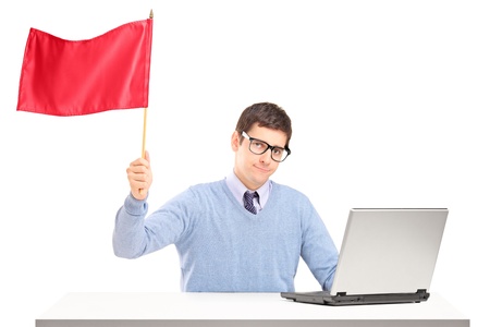 Sad man sitting with laptop and waving a red flag isolated on white backgroundの写真素材
