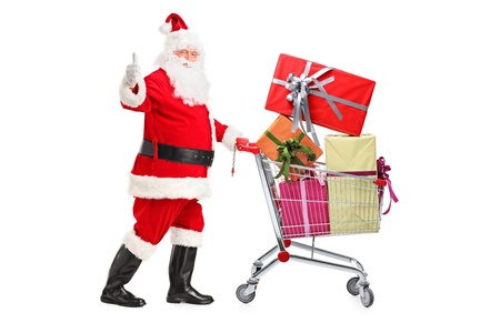 Santa Claus pushing a shopping cart full of gifts and giving a thumb up isolated on white backgroundの写真素材