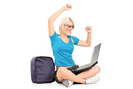 A happy female student seated on a floor working on a laptop isolated on white backgroundの写真素材