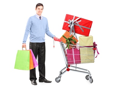 Full length portrait of a young male posing next to a shopping cart full of gifts isolated on white backgroundの写真素材