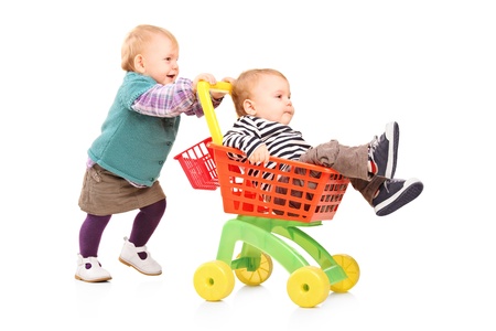 Toddler girl pushing her twin brother in a toy cart isolated on white backgroundの写真素材