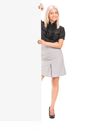 Full length portrait of a smiling woman posing next to a blank panel isolated on white の写真素材