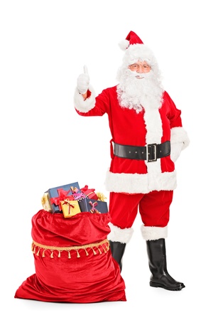 Full length portrait of a Santa Claus with a bag full of gifts giving a thumb up isolated on white backgroundの写真素材