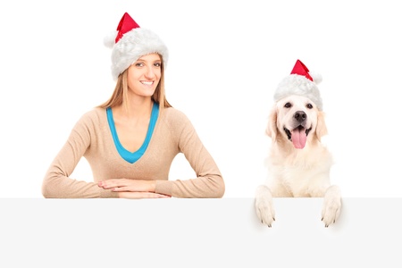 Smiling female and dog wearing santa claus hats and posing behind a blank panelの写真素材