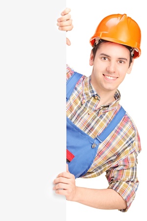 Young construction worker with helmet posing behind a blank panel isolated on white backgroundの写真素材
