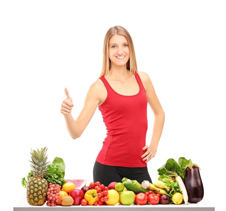 Female athlete giving thumb up behind a table full of healthy food isolated on white backgroundの写真素材
