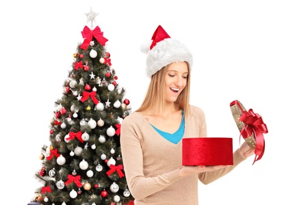Excited female with christmas hat opening a gift and decorated christmas tree in the backgroundの写真素材