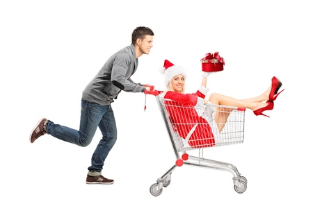 Happy guy pushing a female wearing christmas costume in a shopping cart isolated on white background の写真素材