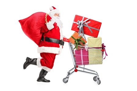 Santa Claus carrying a bag and pushing a shopping cart full of gifts isolated on white backgroundの写真素材