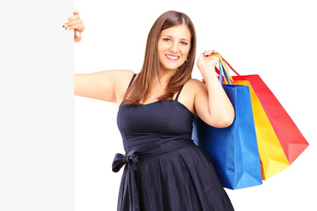 A smiling woman holding a shopping bags behind a white panel isolated against whiteの写真素材