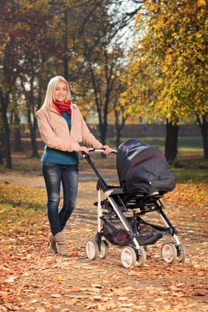 A young mother pushing a baby stroller in a park in autumnの写真素材