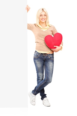 Full length portrait of a young female holding a blank panel and red heart isolated against white backgroundの写真素材