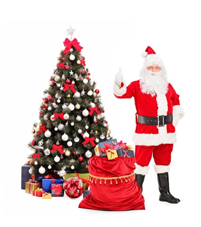 Full length portrait of Santa Claus giving thumb up, a christmas tree in the backgroundの写真素材