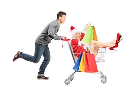 Happy guy pushing a female wearing christmas costume in a shopping cart isolated on whiteの写真素材