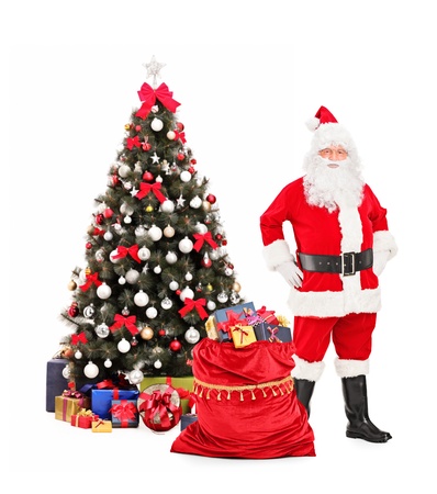 Full length portrait of a Santa Claus standing next to a Christmas tree isolated on white backgroundの写真素材