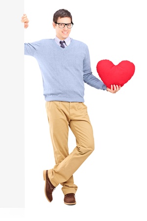 Full length portrait of a young male holding a blank panel and red heart isolated against white backgroundの写真素材