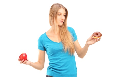 Doubtful woman holding an apple and donut trying to decide which one to eatの写真素材