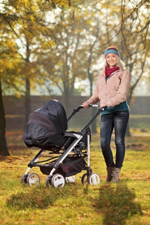 A smiling mother posing with a baby stroller in a park in autumnの写真素材