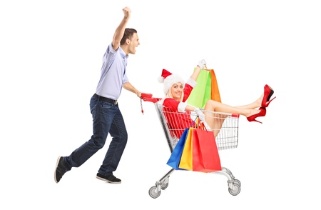 Guy pushing a woman in christmas costume with shopping bags in a push cart isolated on white background の写真素材