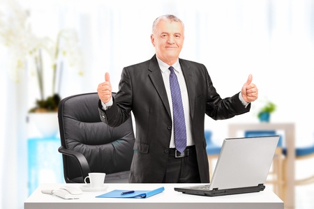 Happy mature businessman standing in his office and giving thumbs upの写真素材