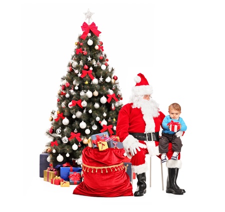 Santa Claus giving a gift to a child in front of decorated christmas treeの写真素材