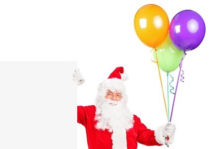 A happy Santa claus standing next to a blank billboard and holding balloons isolated on whiteの写真素材