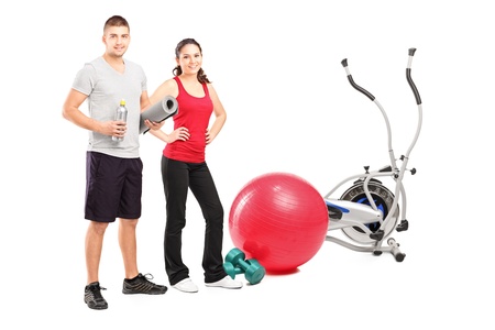 Full length portrait of a male and female athlete posing next to an excerise equipment isolated on white backgroundの写真素材