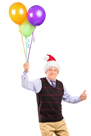 Joyful mature gentleman with christmas hat holding bunch of balloons and giving thumb up isolated on white backgroundの写真素材