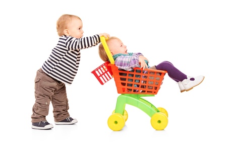 Toddler boy pushing his twin sister in a toy cart isolated on white backgroundの写真素材