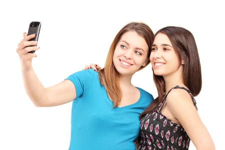 Two happy teenagers taking pictures of themselves with a cell phone isolated on white backgroundの写真素材