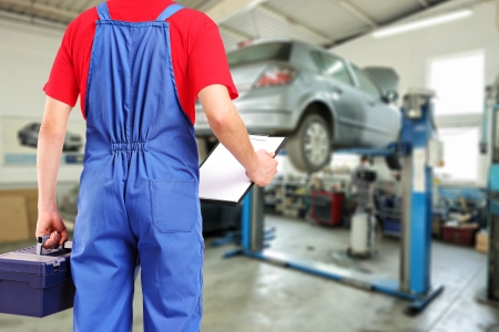 Mechanic with a tool box and clipboard standing in a car repair serviceの写真素材