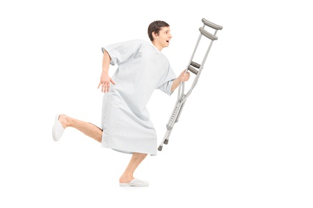 Full length portrait of a male patient running and holding a crutch, isolated on white backgroundの写真素材