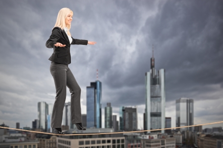 Young businesswoman walking on a rope, with the financial centre in Frankfurt, Germany in the backgroundの写真素材
