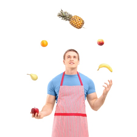 Young man in apron juggling with fruits, isolated on white backgroundの写真素材
