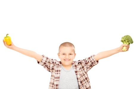 An excited little kid holding broccoli, and a pepper in his hands, arms open wide, isolated on white backgroundの写真素材