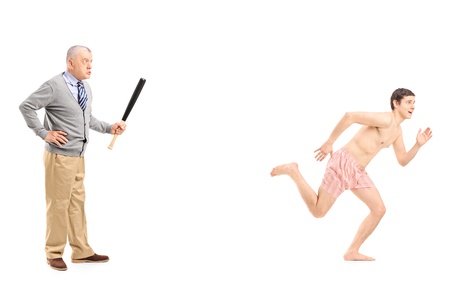 Full length portrait of an angry middle aged man with baseball bat shouting at a naked man running away, isolated on white backgroundの写真素材