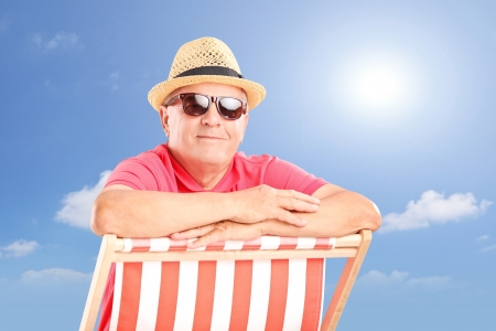 Smiling mature man wearing hat and sunglasses, posing on a beach chair on a sunny dayの写真素材