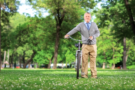 Full length portrait of a mature man with a bicycle in a parkの写真素材