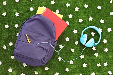 School backpack with books and headphones on a green grass with daisy flowers