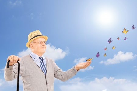 Mature smiling man holding a cane and looking at colorful butterflies on a sunny dayの写真素材