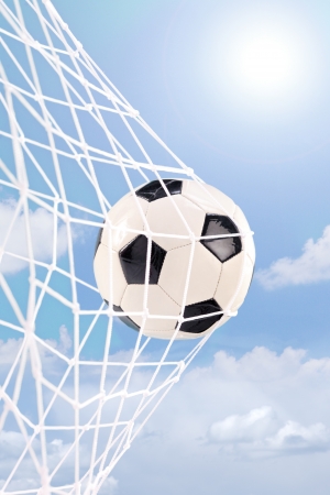 Soccer ball in a goal net against cloudy skyの写真素材