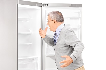 Shocked mature man looking in empty fridge and finding out there is no food, isolated on white backgroundの写真素材