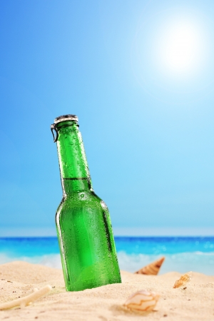 A view of a beer bottle on a sandy beach, with clear sky and sun, next to the sea の写真素材